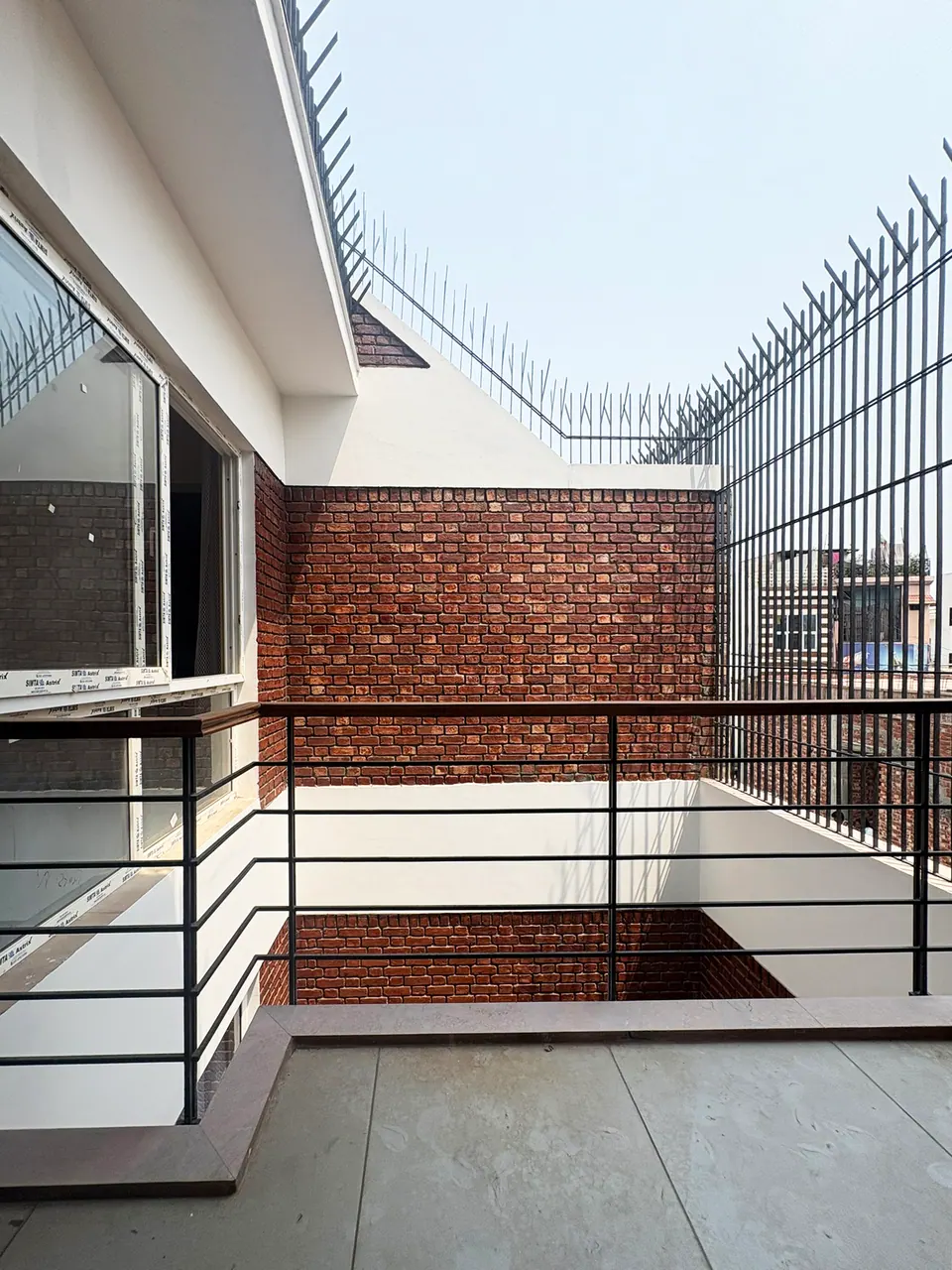 Upper balcony with a black steel railing overlooking the courtyard void, brick walls and a spiked steel grille above