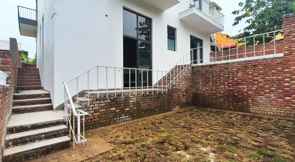 White-rendered elevation above brick retaining walls, with stairs climbing past a sloping lawn