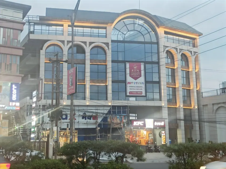 Commercial block at dusk with lit arched bays around a central arched glass window, trees and overhead wires in front