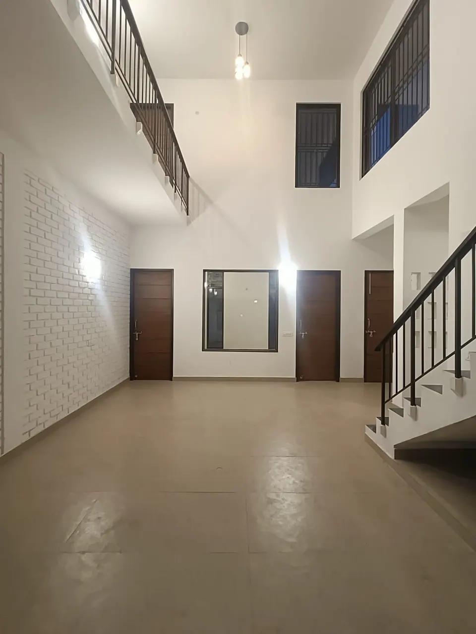 Double-height hall: a gallery with a black railing above, white-painted brick walls, timber doors and the foot of the stair