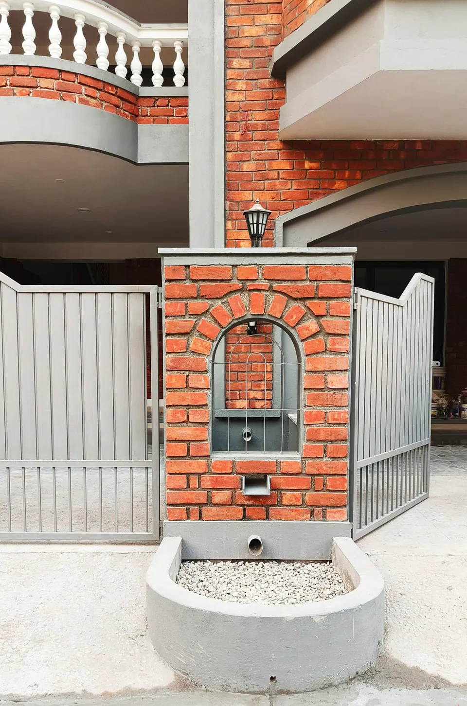 Brick gate pier with an arched niche and a lamp, above a curved planter of white pebbles