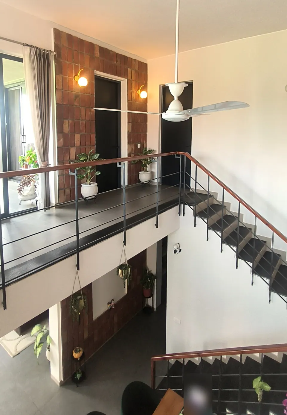 Upper gallery with a timber handrail and steel balusters crossing the double-height space, a brick-tile wall and doors
