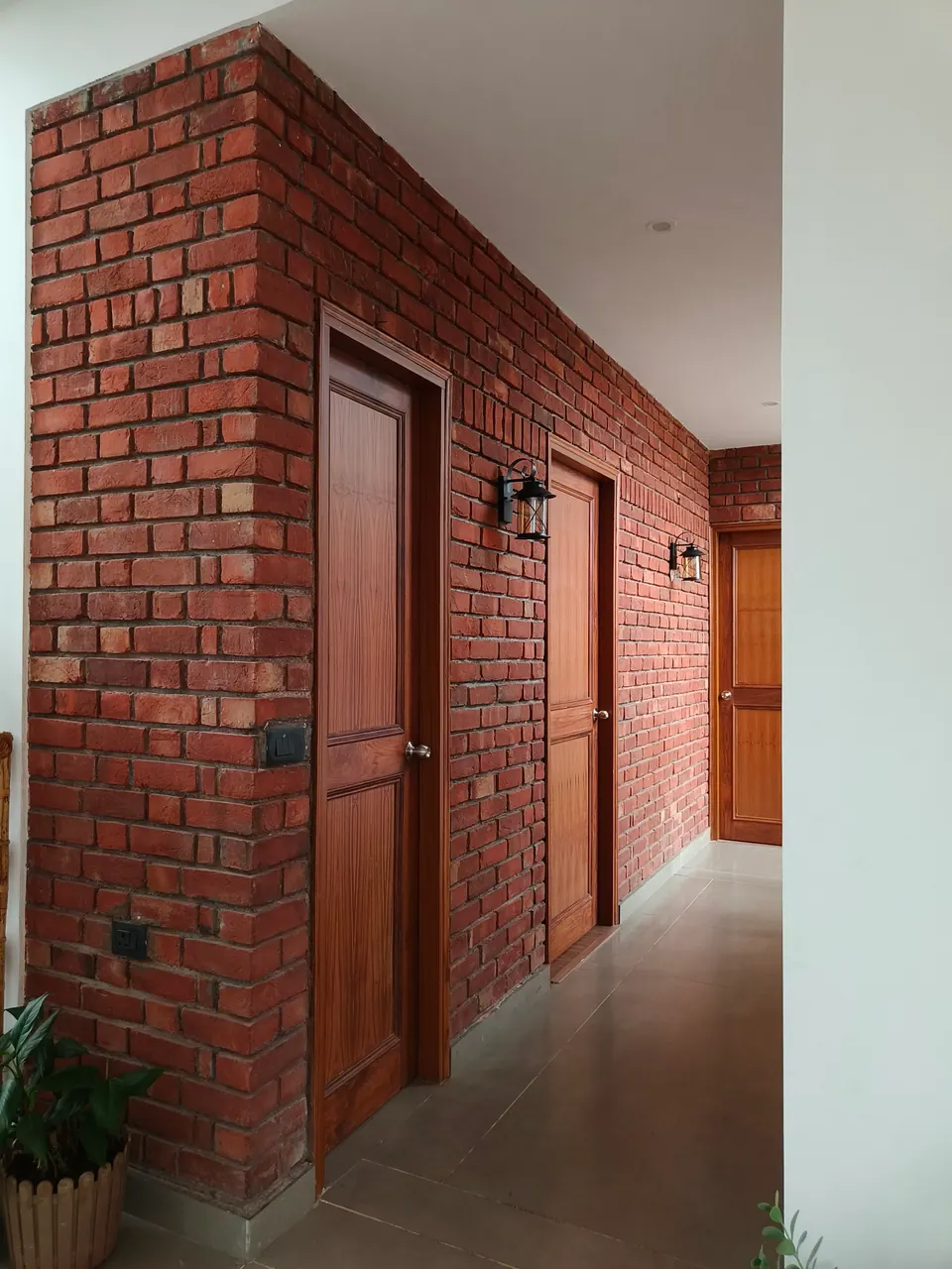Corridor along an exposed brick wall with timber doors and black wall lanterns