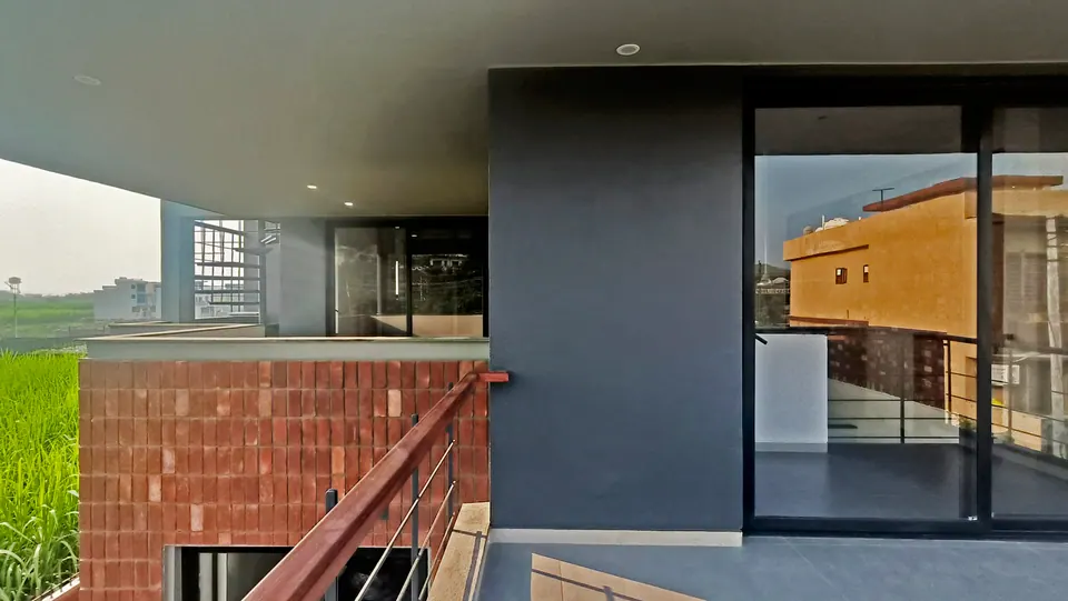 Upper terrace with a dark grey wall, a timber handrail and glazed doors, brick cladding below and fields beyond