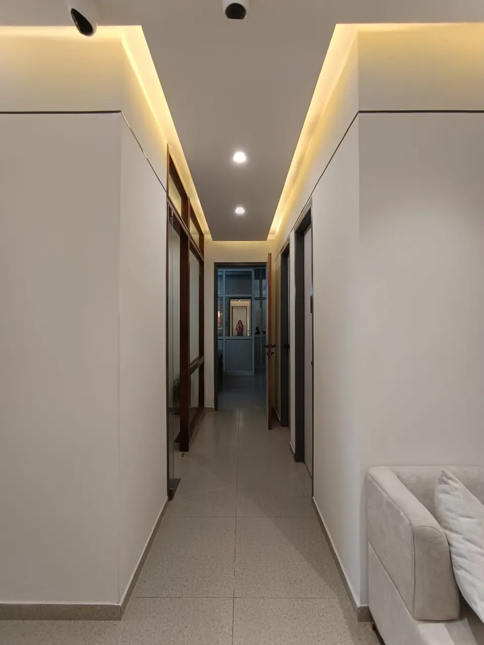 Narrow corridor with cove lighting, white walls and timber-framed glazed doors