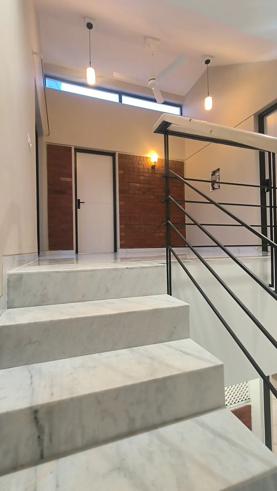 Wide marble stair rising to a landing with brick-clad walls, white doors and pendant lights