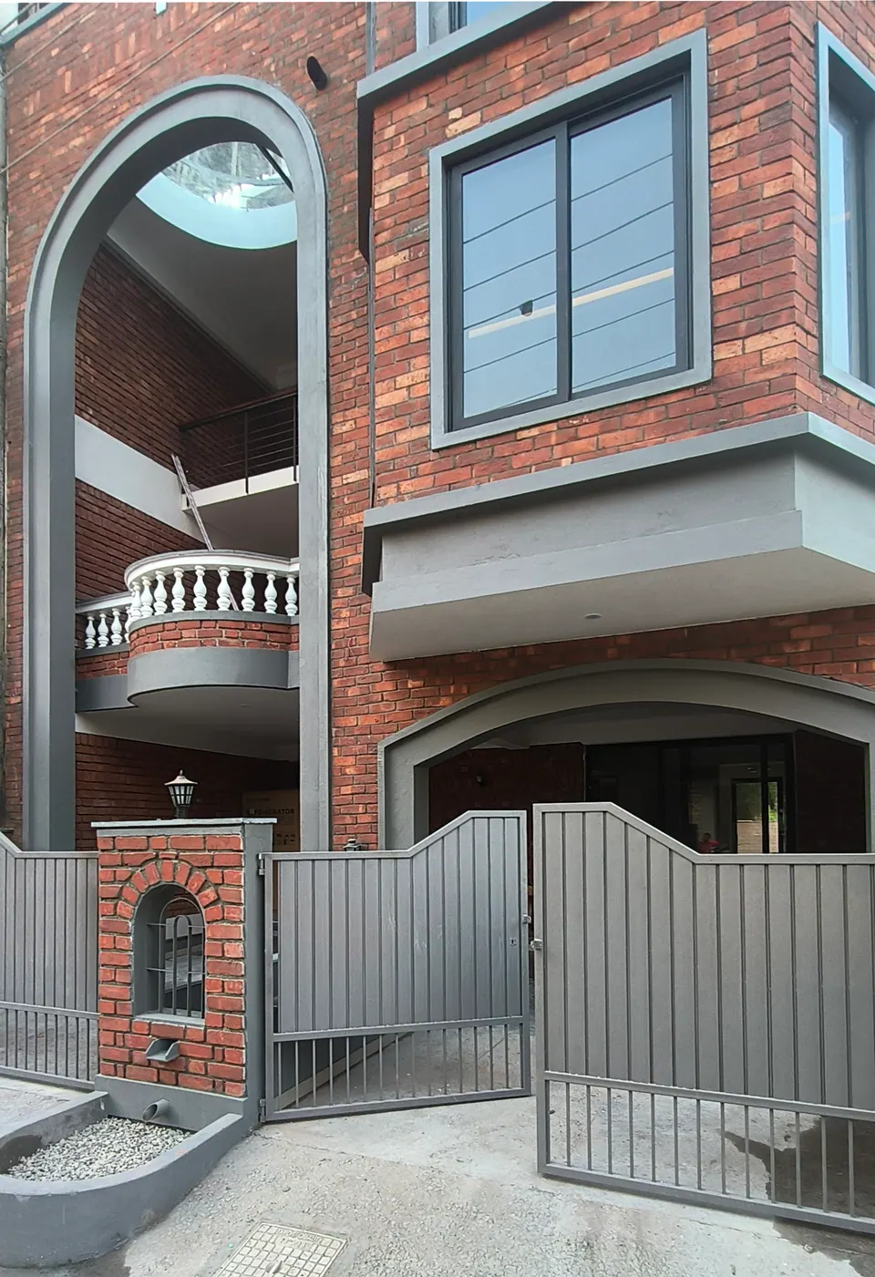 Grey gate beside a brick gate pier with an arched niche, the tall arch and a balustraded balcony above
