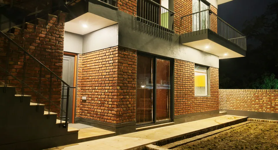 Brick house at night: steel stair, cantilevered balconies and lit soffits over grey bands and glazed doors