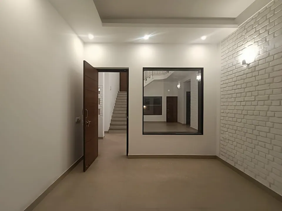 Room with a white-painted brick wall and wall light, an open timber door and a large internal window onto the stair hall
