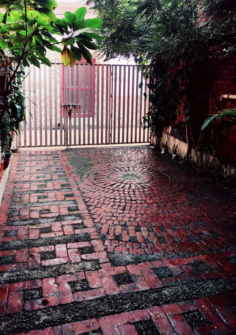 Courtyard paved in red brick and gravel in circular and key patterns, leading to a white steel gate