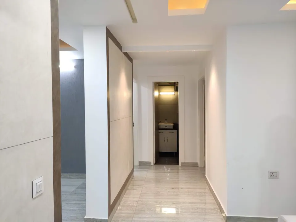 White corridor with a marble floor and timber-edged wall panels leading to a lit washroom door