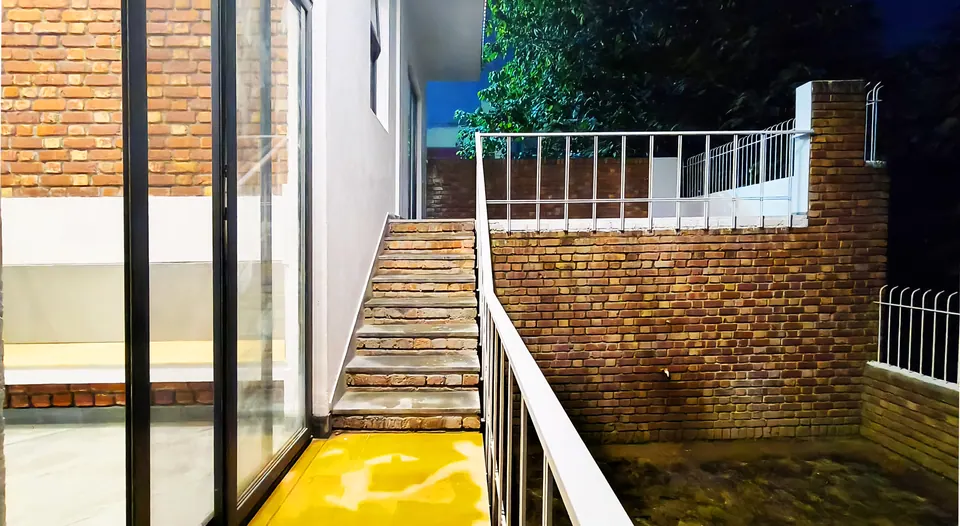 Night view from a glazed door to steps rising between brick retaining walls with white railings
