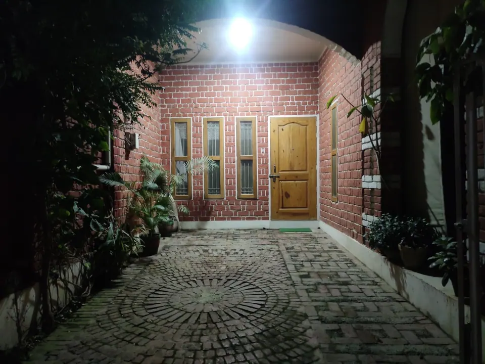 Forecourt at night: lamplight on red brick walls, the timber door and slim windows, and the circular paving