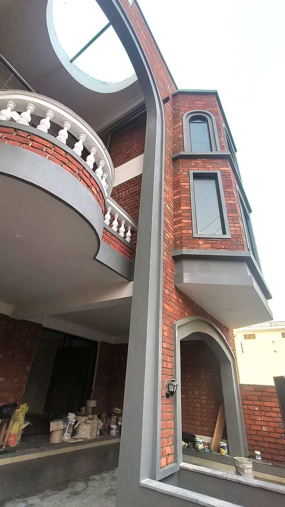 Upward view of the tall grey arch beside a curved white balustraded balcony and a brick bay with slim windows