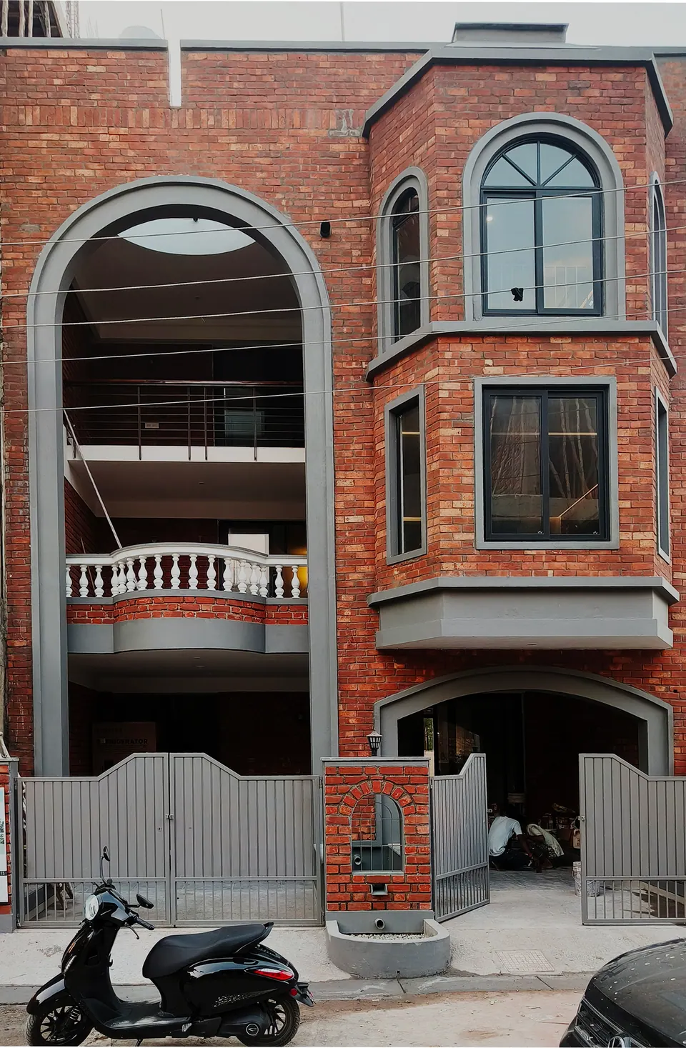 Brick facade with a full-height grey arch framing balconies, a bay window with an arched top and a balustraded balcony