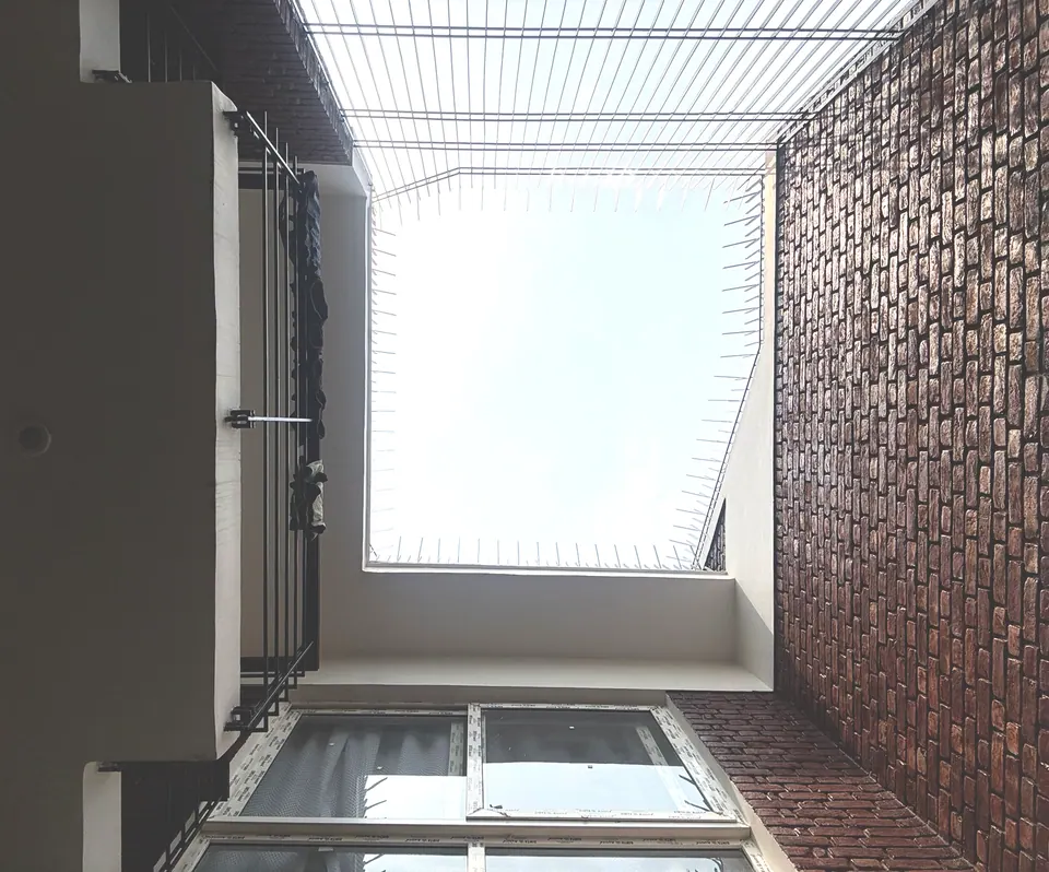 View up through the open-to-sky courtyard: a brick wall, a white slab edge and a steel grille against the sky