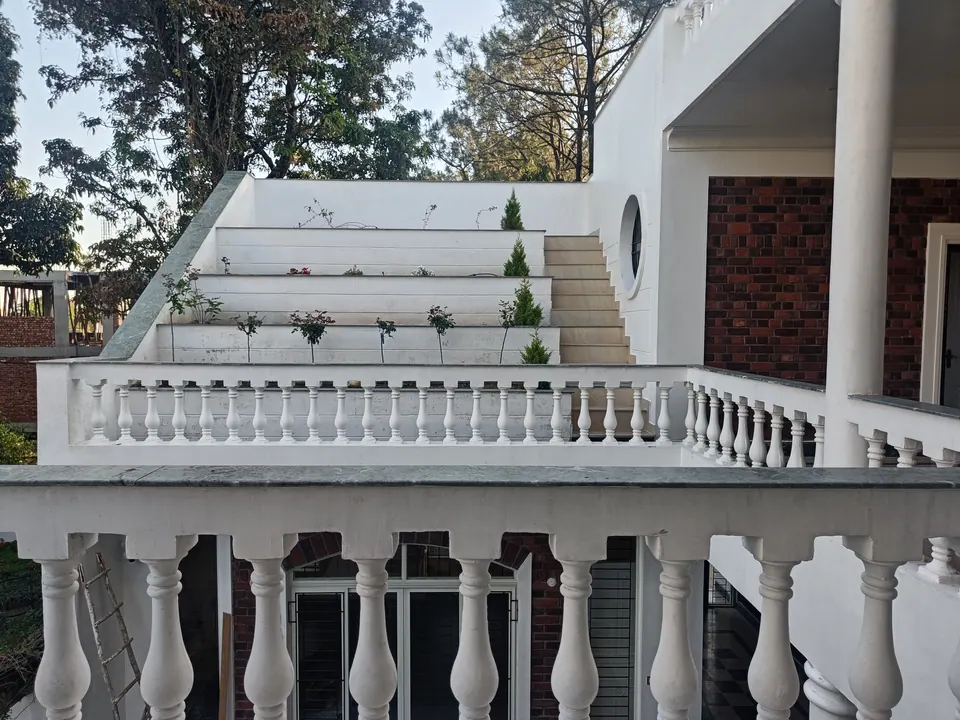 Stepped white terraces with young plants rising behind a balustrade, beside a white column and an exposed-brick wall