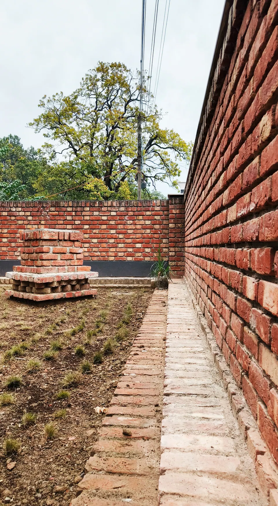 Lawn strip with brick edging along the tall brick boundary wall, a brick plinth planter at the far end