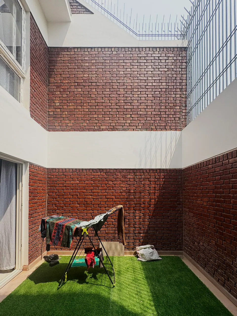 Inner courtyard with artificial turf, enclosed by exposed brick walls and a white upper band, with a drying rack in use