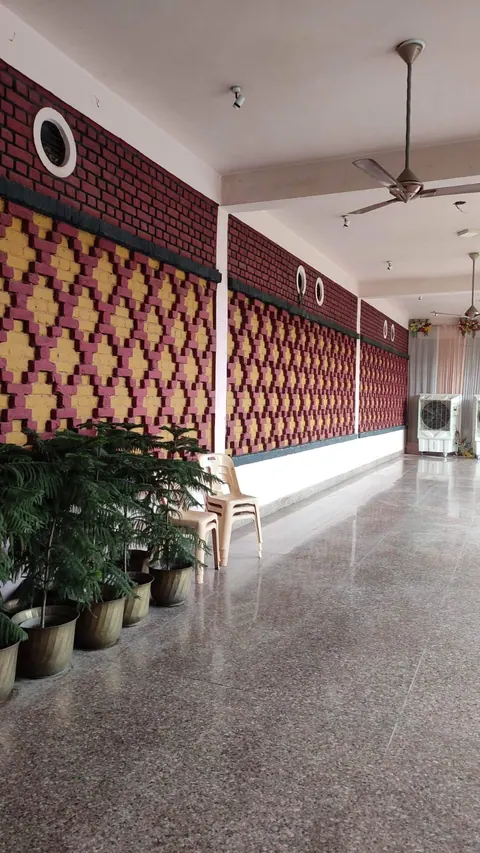 Corridor with a terrazzo floor and potted plants beside a red-and-yellow patterned brick wall with round openings above