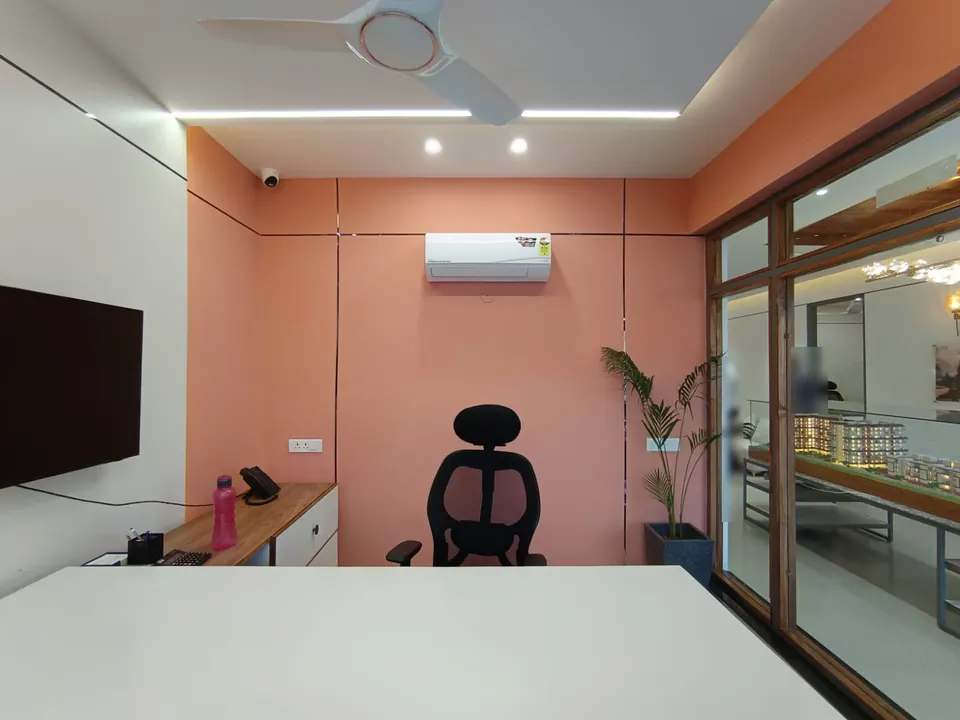 Cabin with coral walls, a white desk and black chair, and a glass partition onto the lit scale model of the housing