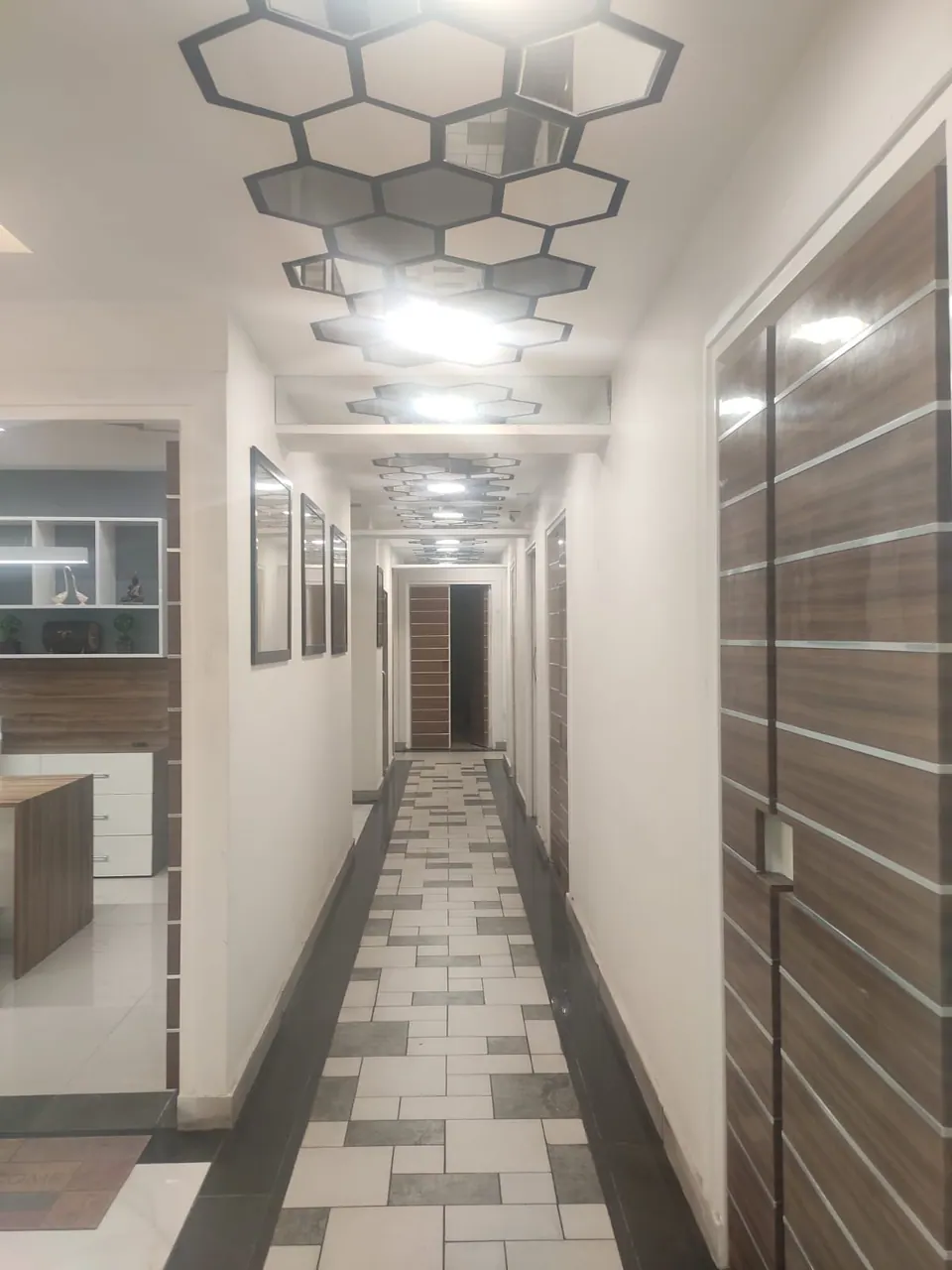 Corridor with a patterned tile floor, framed prints and timber-and-steel striped doors under hexagonal ceiling panels