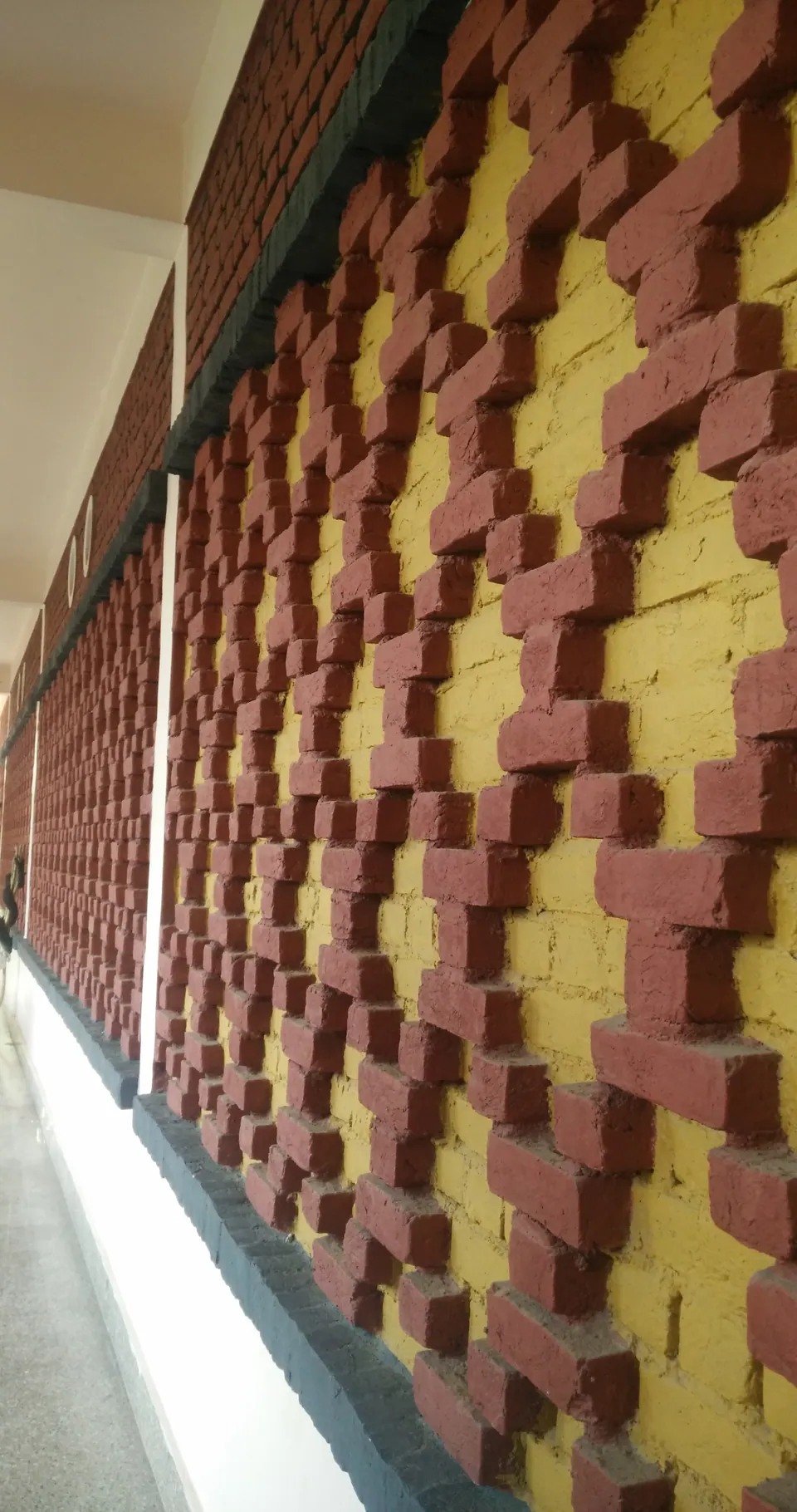 Close view of a patterned brick wall: projecting red and yellow bricks forming a diamond motif along a corridor