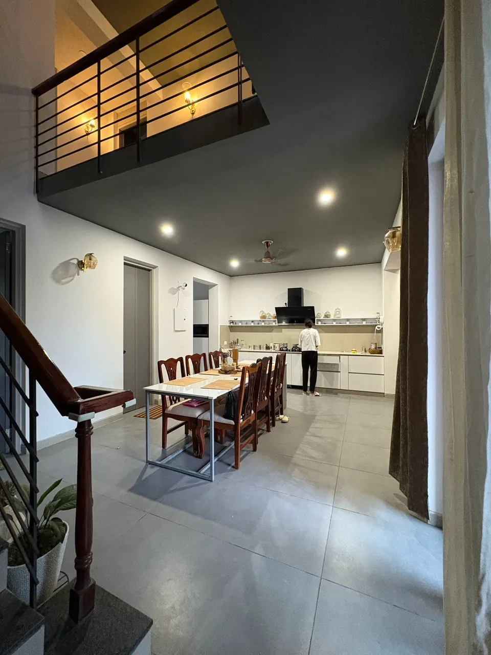 Upper landing railing above a dining area with a long table and an open kitchen beyond