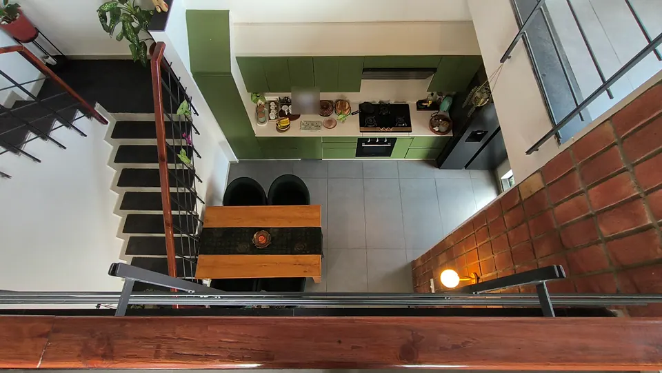 Top-down view from the gallery rail into the kitchen and dining area: green cabinets, a hob and a teak table