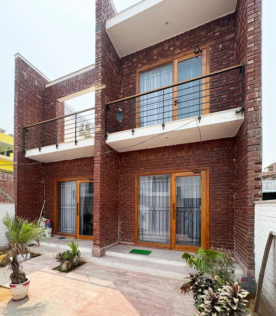 Brick facade seen from the forecourt: two balconies with black steel railings above timber-framed glazed doors and potted plants