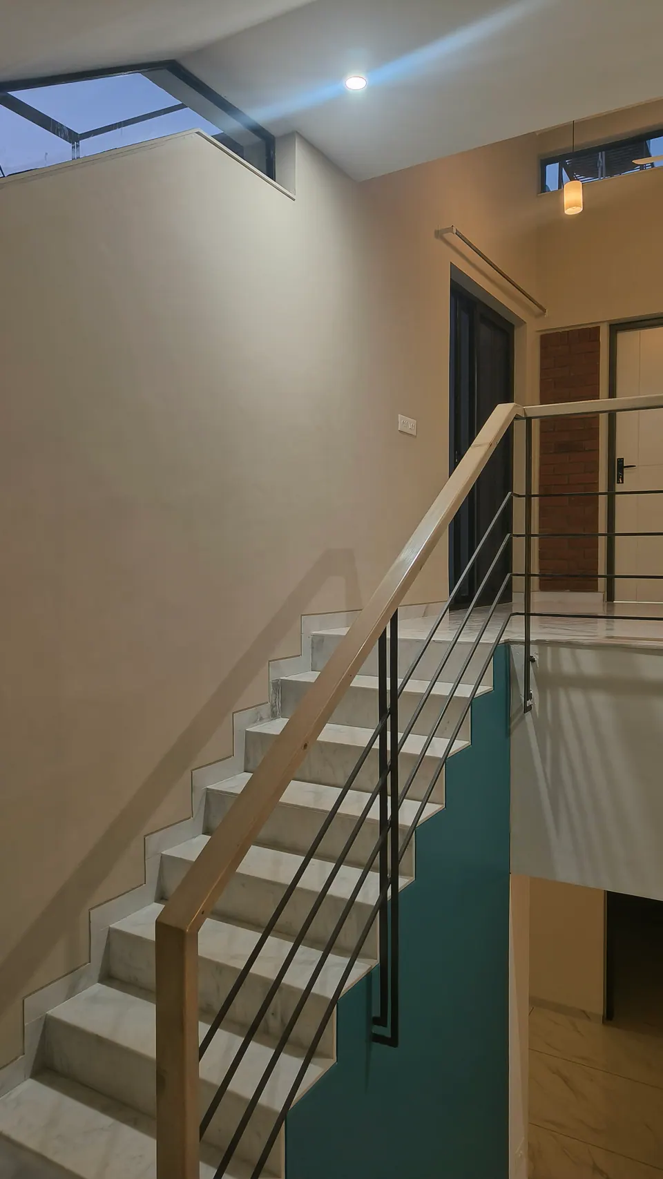 Marble stair with a timber handrail and black balusters rising to a landing, a teal wall and a skylight above
