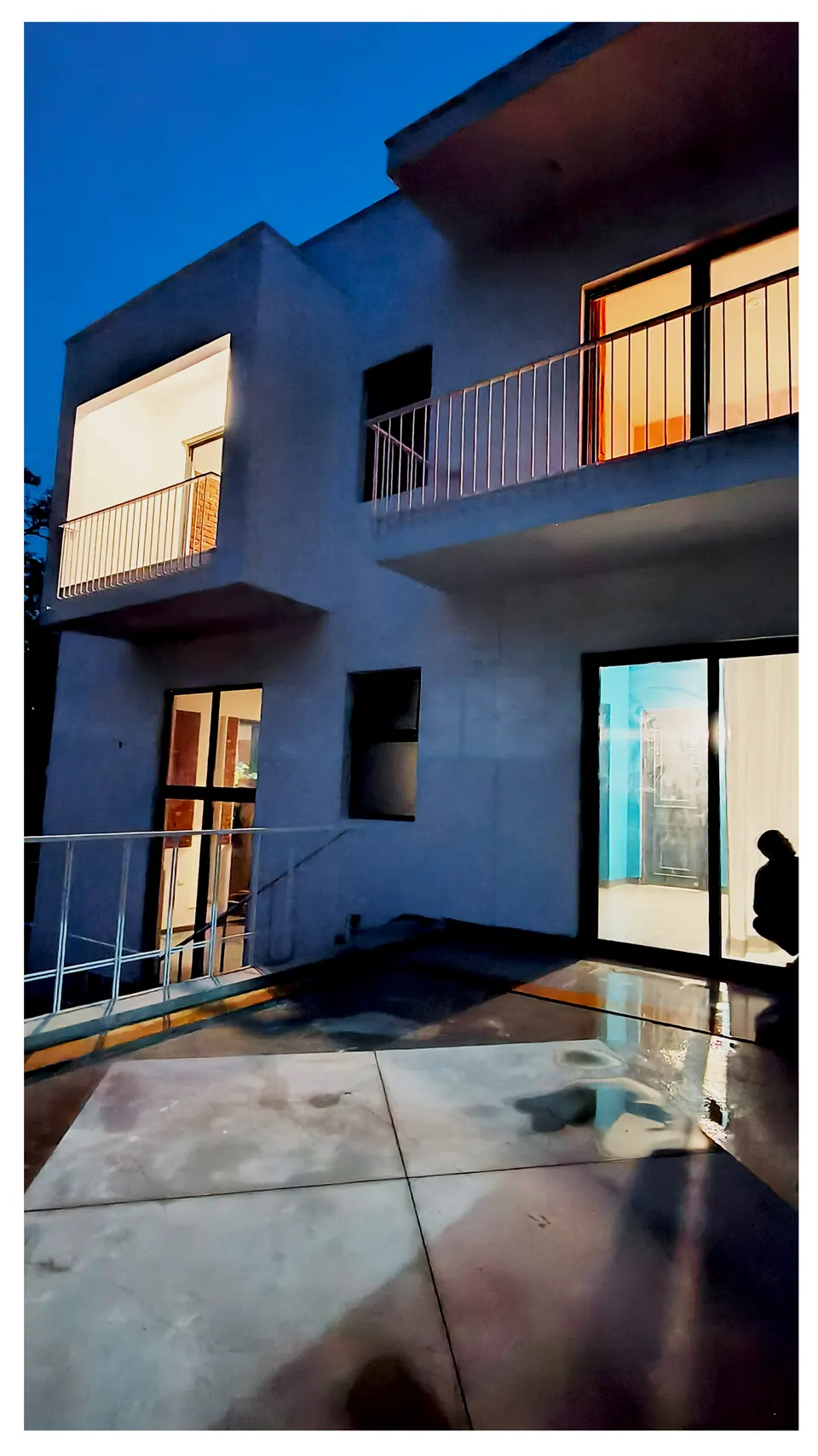 Elevation at night with lit balconies above a wet terrace and a glazed sliding door