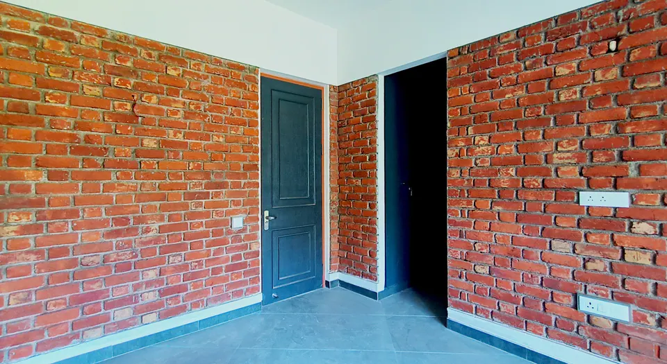 Room with exposed brick walls, a dark panelled door and a doorway to the next room
