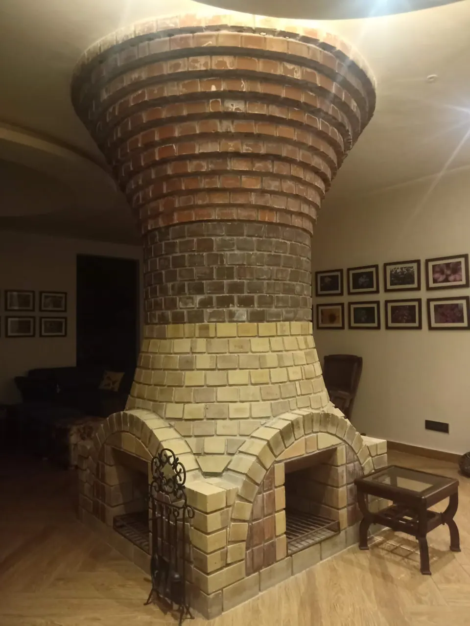 Hourglass-shaped brick chimney rising from arched fireplaces in pale brick to a dark brick flue at the ceiling