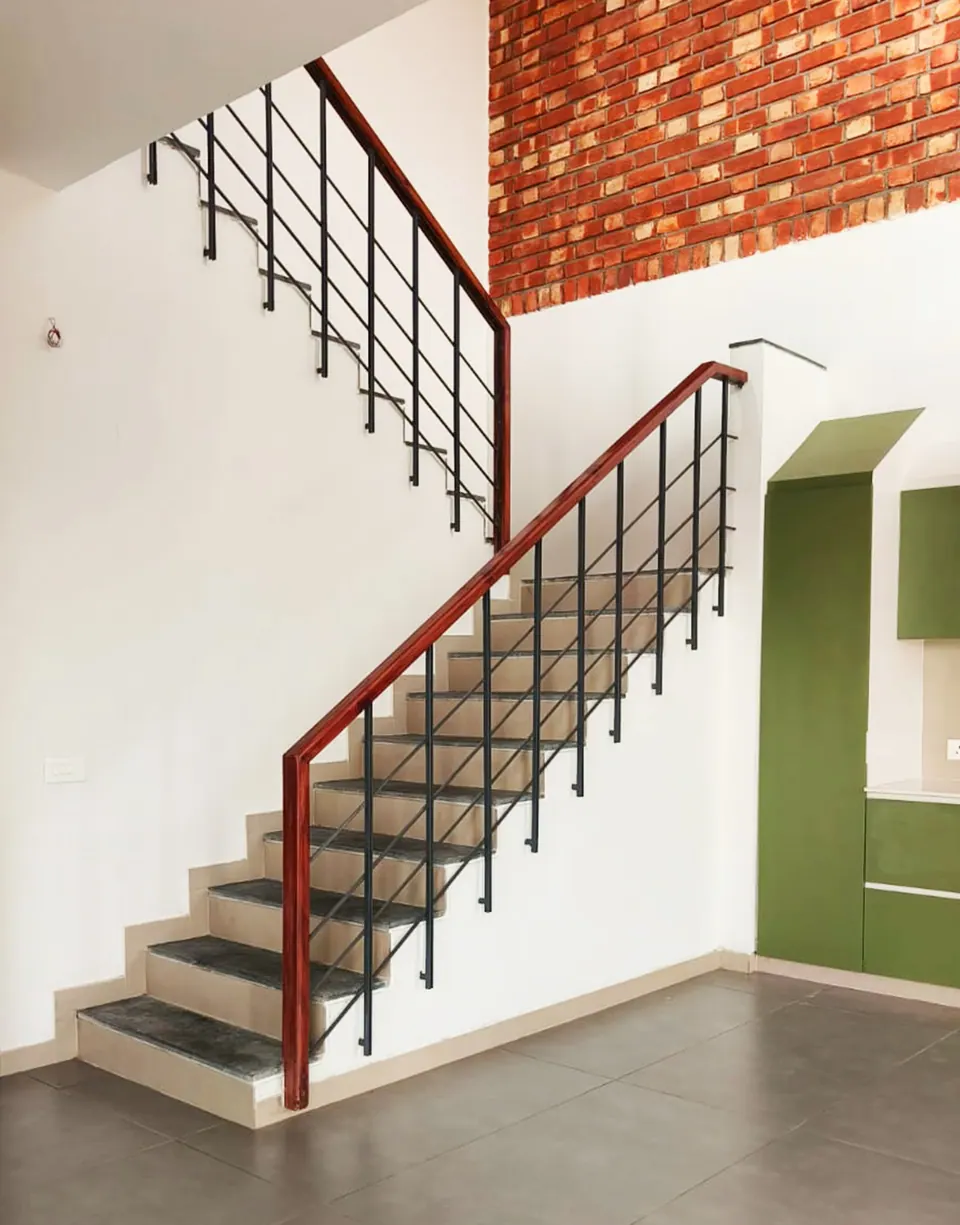 Stair with slate-faced treads, steel balusters and a timber handrail, a brick wall above and the green kitchen beside