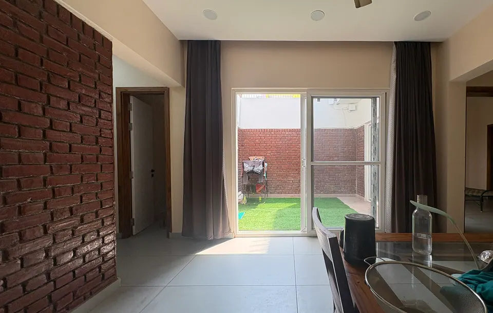 Dining area beside an exposed-brick wall, looking through a sliding glass door to the turfed courtyard