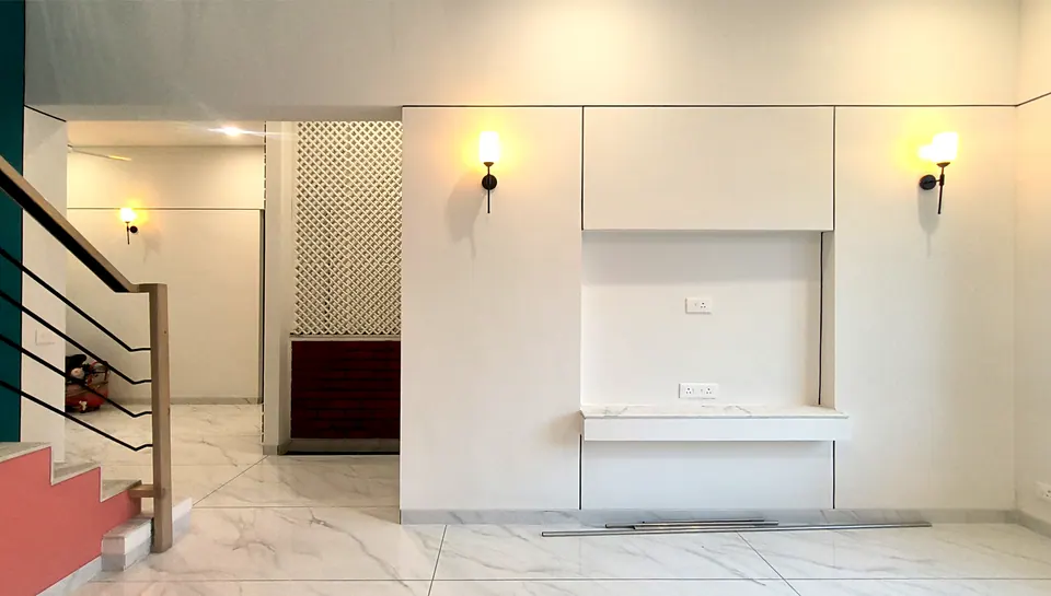 Living area with white panelled walls, wall lamps and a floating marble ledge, a lattice screen and the stair at left