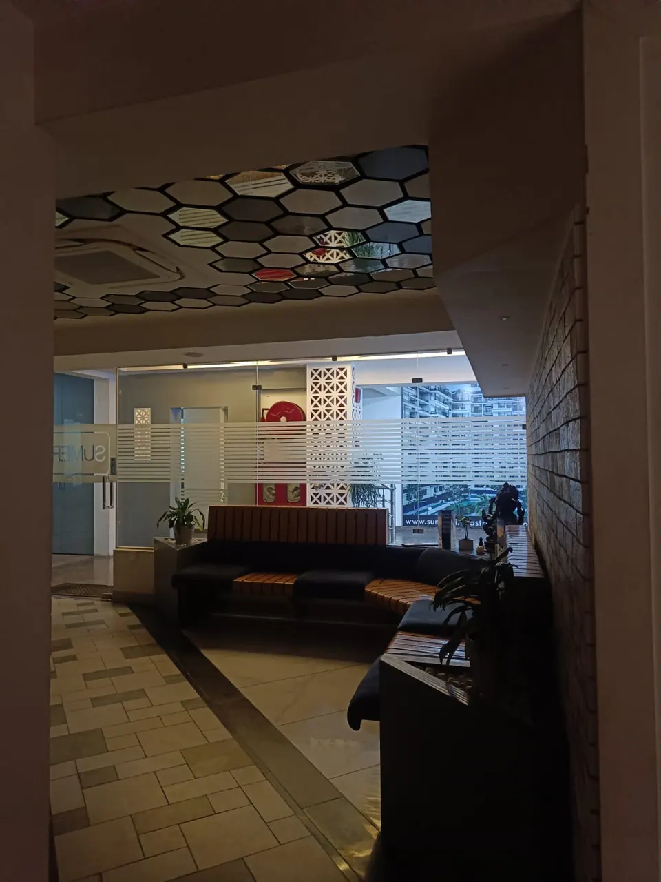 Doorway view at night into the lounge with the curved sofa under a hexagonal ceiling and a white lattice screen