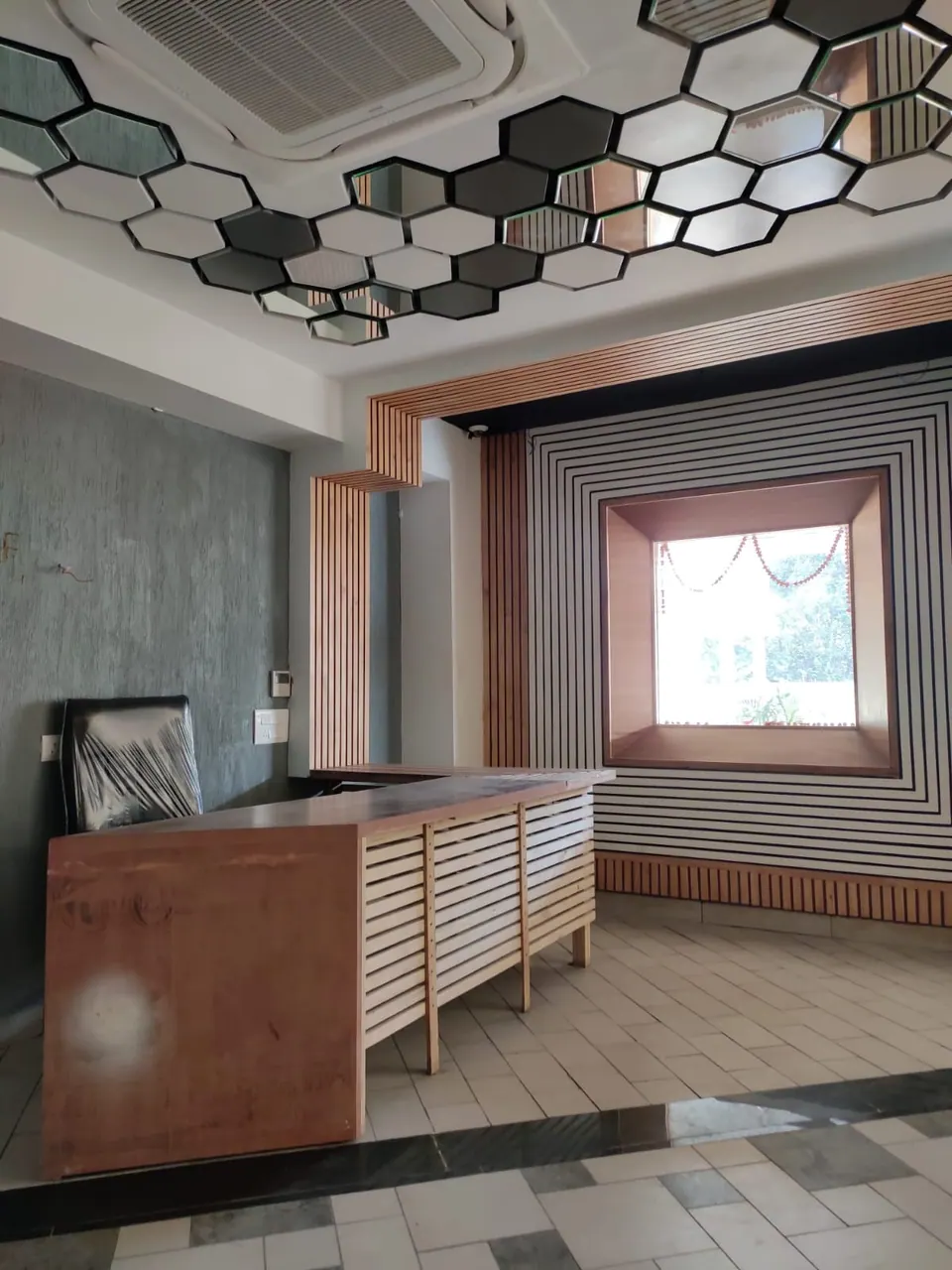 Desk with a timber-slatted front before a wall of black and white concentric stripes framing a timber-lined window