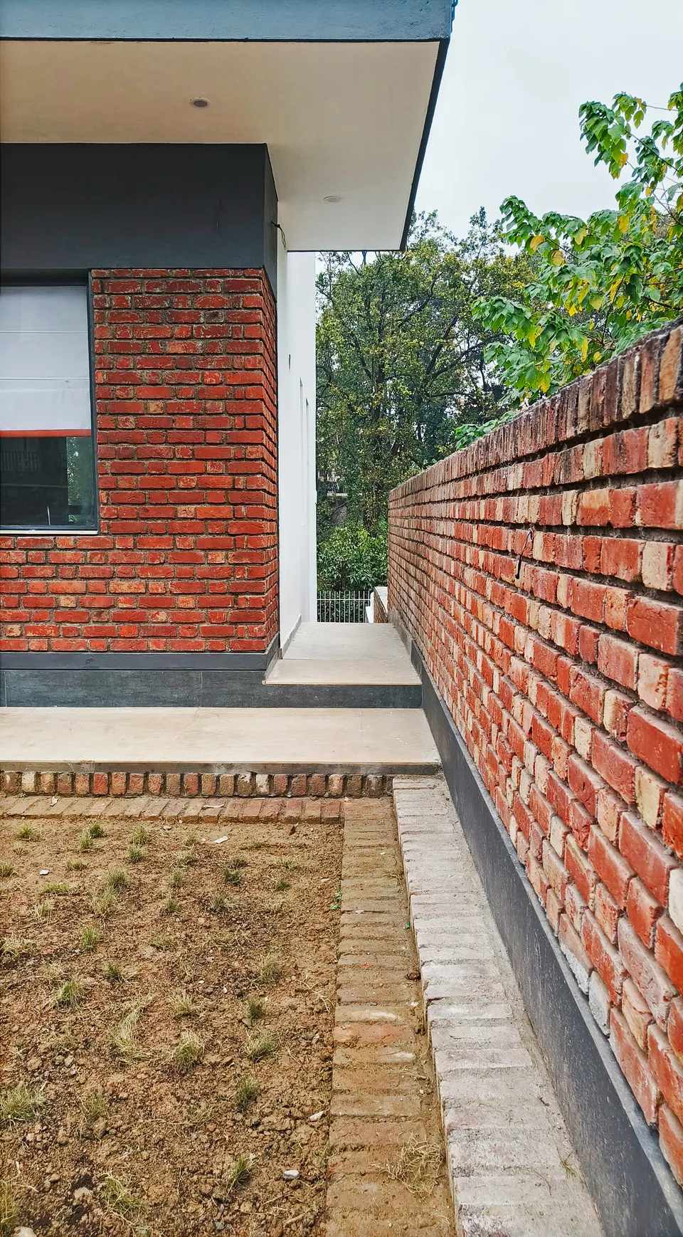 Side passage between the house and a tall brick boundary wall, with a lawn strip edged in brick