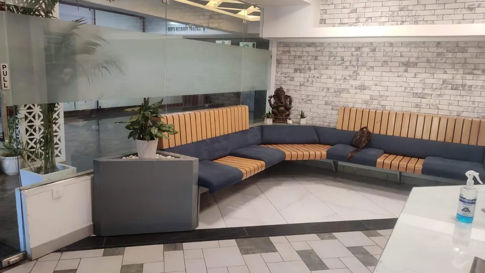 Lounge with a curved blue sofa and timber-slatted back, a planter, a brick-effect wall and a frosted glass partition