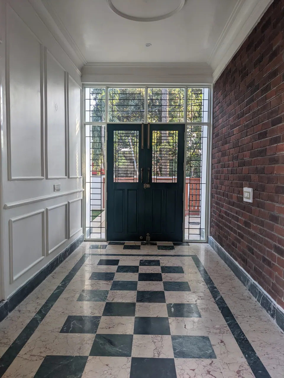 Entrance lobby: a black and white chequered marble floor, panelled white walls, an exposed-brick wall and dark green double doors