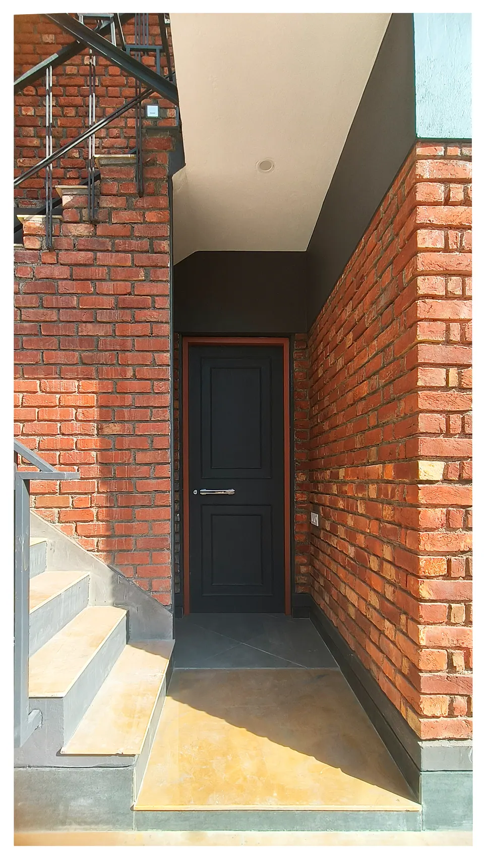 Dark entrance door set deep in a recessed brick niche, with steps and a steel railing to the left