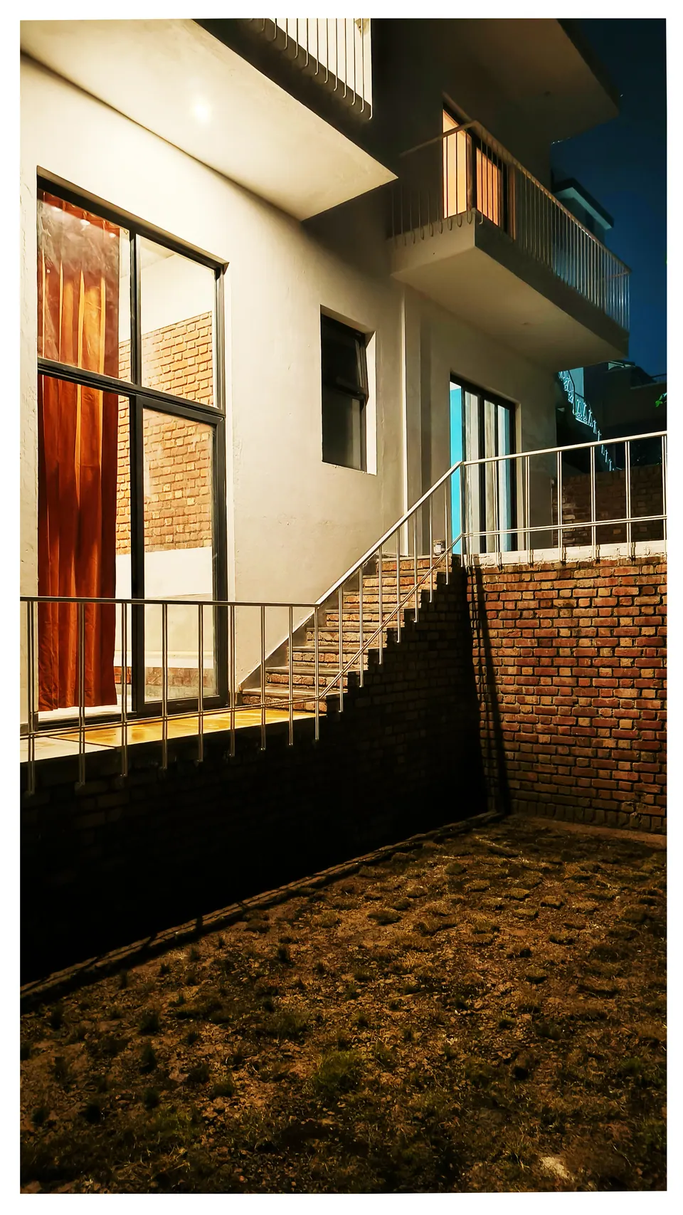 Night view of a timber-framed door, a stair along a brick retaining wall and a dark lawn