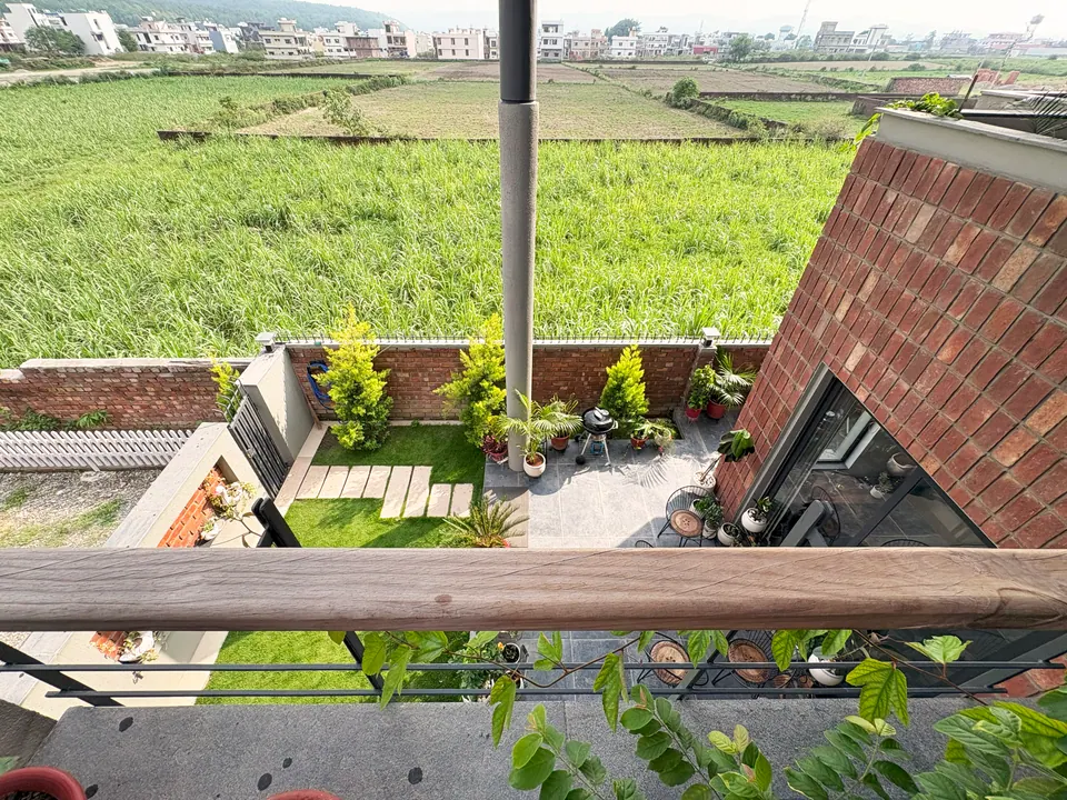 View from a timber-railed balcony down to the garden, patio and brick-clad block, with fields beyond