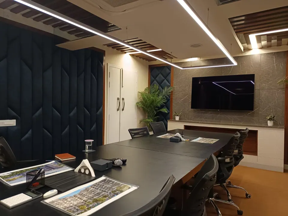 Conference room with a long black table, navy upholstered wall panels, a stone-clad TV wall and linear ceiling lights