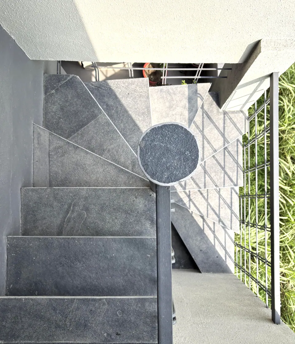 Grey stone spiral stair seen from above, with a round newel cap and a steel mesh screen carrying climbers