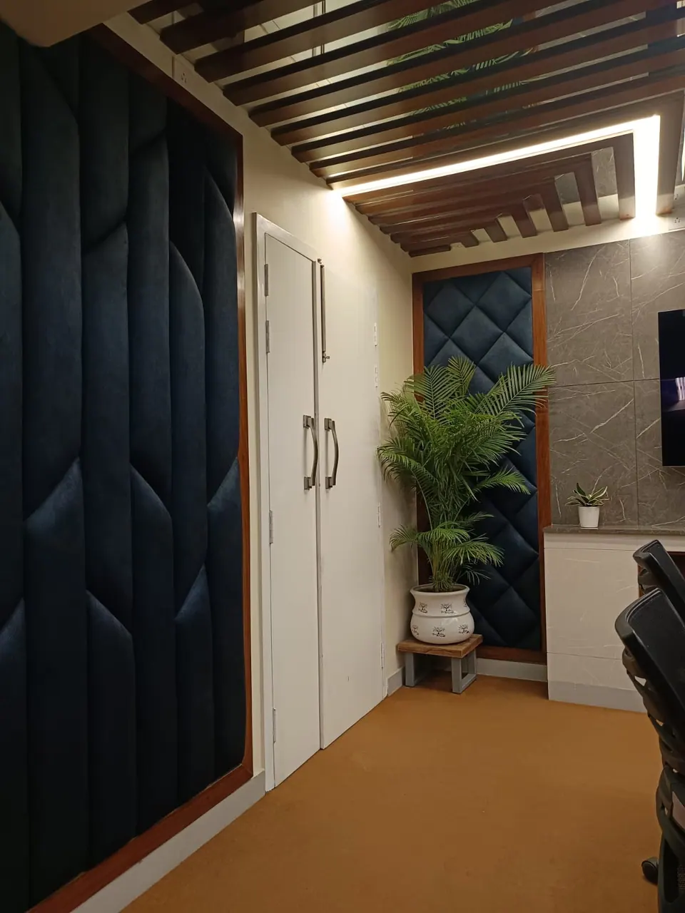 Corner of the conference room with navy quilted wall panels, white cupboard doors and a potted palm on carpet