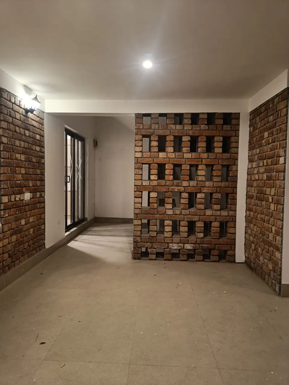 Room with exposed-brick walls and a perforated brick jali screen opening onto a passage
