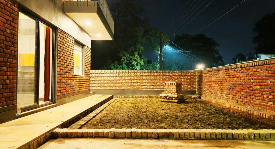 Walled garden at night: lawn edged in brick, a brick plinth planter and a tall brick boundary wall